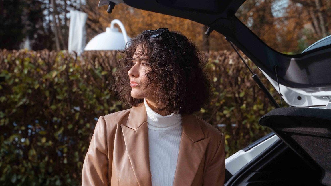 Комплексне страхування Молода жінка стоїть перед відкритим багажником свого автомобіля