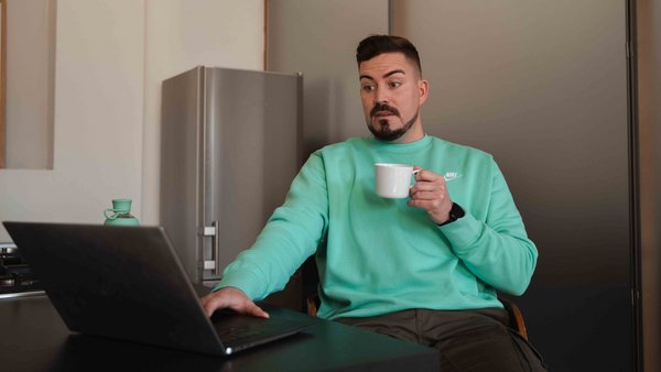 Страхування вашого автомобіля Чоловік сидить перед ноутбуком із чашкою в руці, приголомшений