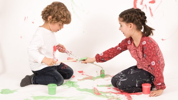 Наші послуги Двоє дітей сидять на підлозі та малюють разом.